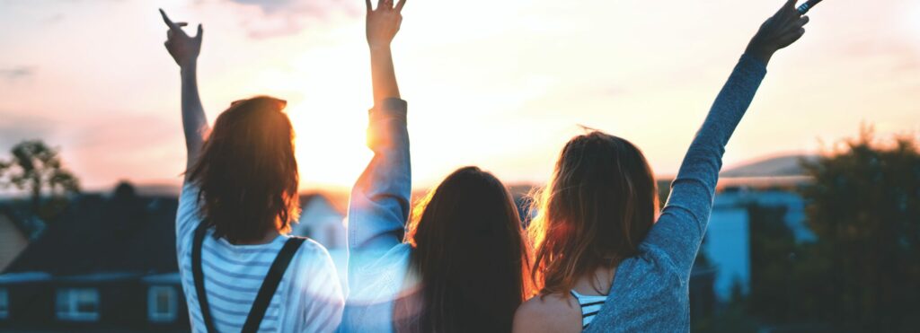 Three girls with their hands raised, watching the sunset